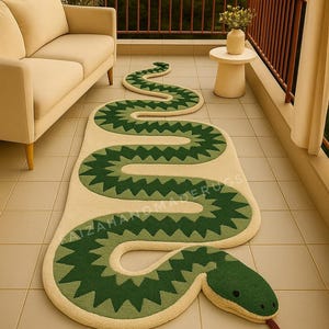May include: A beige and green snake-shaped rug with a detailed design. The rug features a light beige body with dark green zigzag patterns and a green head with a red tongue. The rug is placed on a tiled floor.