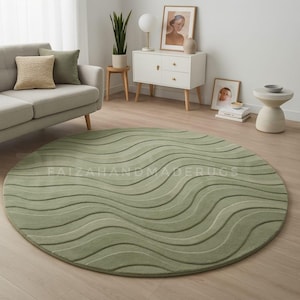 May include: A circular, sage green rug featuring a wave-like design. The rug is made from a soft material and has a textured appearance. It's positioned on a light wood floor, creating a cosy living room atmosphere.