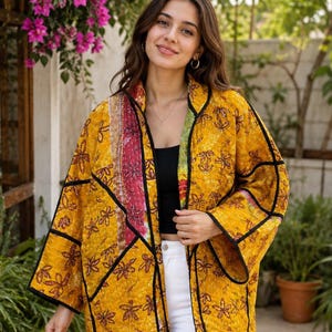 Peut inclure: Une veste matelassée d'un jaune moutarde vif avec un motif floral répétitif marron foncé. Le vêtement est rehaussé d'un liseré noir sur les bords et d'un panneau vertical de broderies kantha multicolores sur le côté gauche.