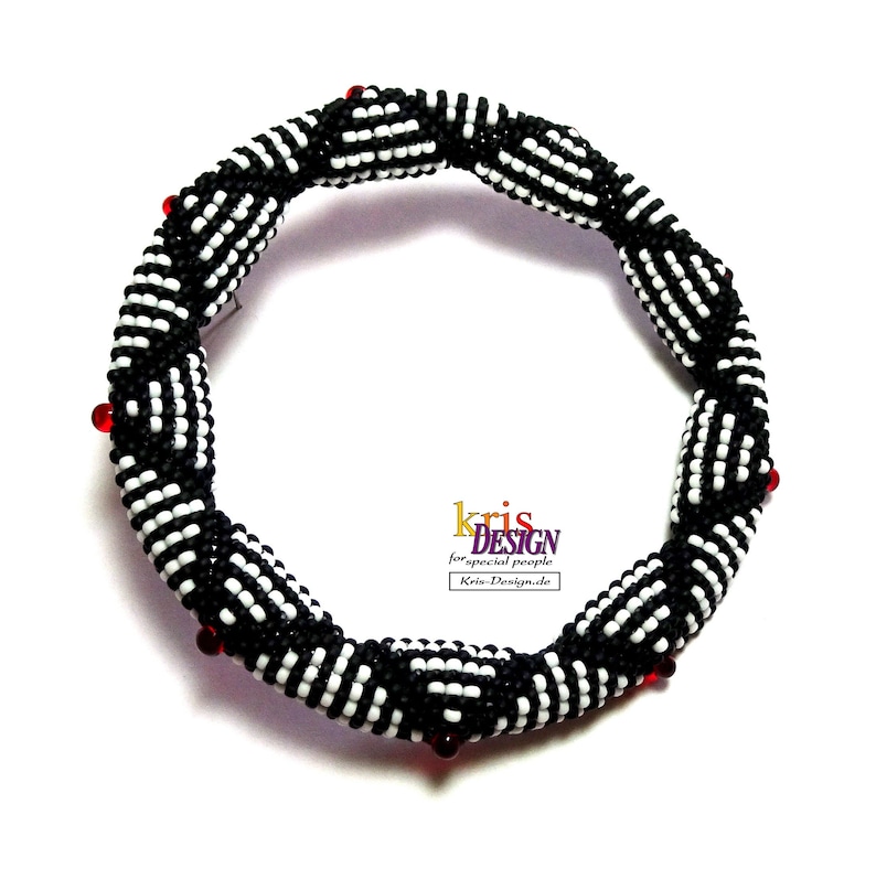 May include: Black and white beaded bracelet with red beads. The bracelet is made of small, round beads that are woven together in a pattern. The bracelet is about 7 inches in diameter.