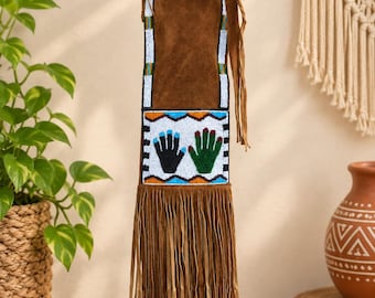 May include: A brown suede pouch featuring long fringe at the bottom and a beaded panel. The panel displays two hand prints, one black and one green, surrounded by white, blue, and orange geometric beadwork patterns and vertical beaded borders.