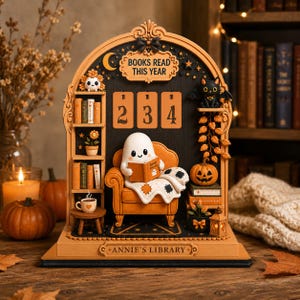 May include: An arched wooden display titled BOOKS READ THIS YEAR and ANNIE'S LIBRARY featuring a ghost sitting in an orange armchair reading a book. The display includes a bookshelf, a black cat, a pumpkin, a coffee mug, and numbered cards 2, 3, 4.