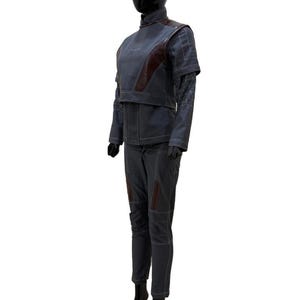 May include: A gray and burgundy two-piece outfit displayed on a mannequin. The outfit includes a high-collared jacket with burgundy accents and matching pants. White stitching details the seams. The mannequin is black and stands on a black base.