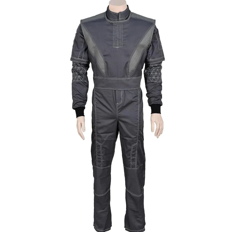 May include: A gray jumpsuit with a high collar and long sleeves. The suit features light gray accents on the shoulders, chest, and sleeves, with white stitching details. Black cuffs are visible at the wrists. The jumpsuit is displayed on a mannequin.