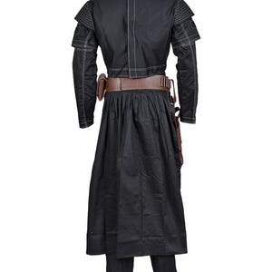 May include: Black costume with white stitching. The outfit features a long-sleeved jacket, a long skirt, and matching trousers. A brown belt and holster are also included. The costume is designed with a unique, layered construction.