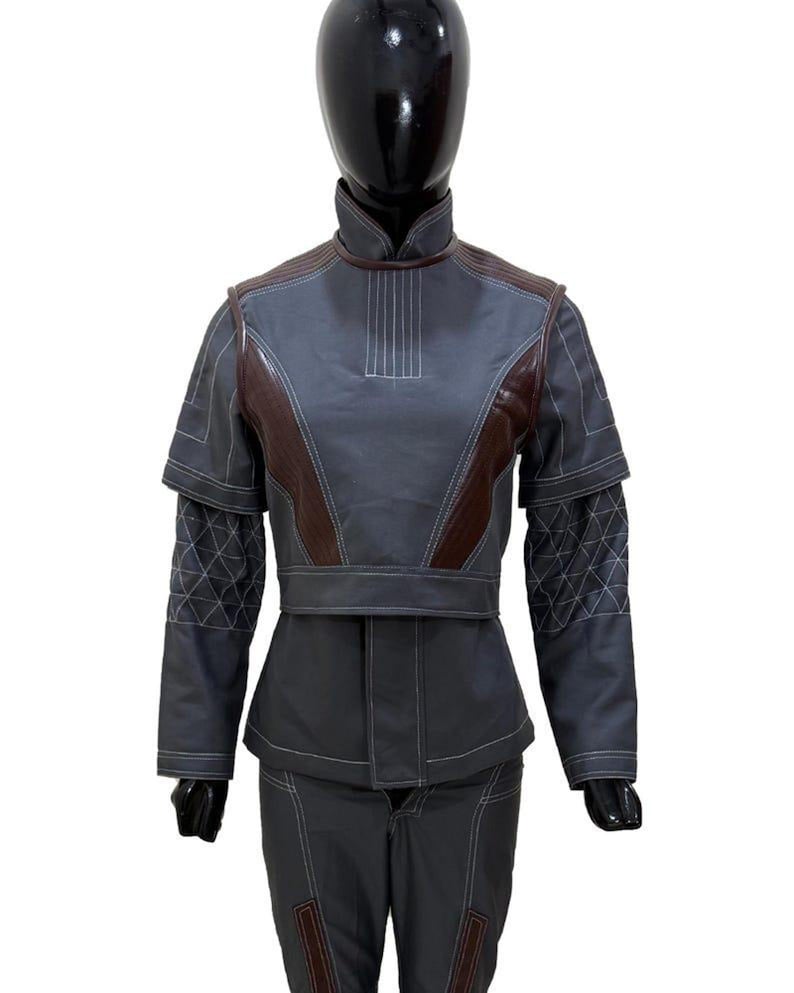 May include: A gray and brown two-piece outfit. The jacket has a high collar, brown shoulder accents, and white stitching details. The sleeves feature a diamond pattern. The pants have brown accents at the knees.