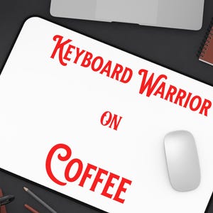 Può includere: Tappetino per mouse rettangolare bianco con la scritta rossa "KEYBOARD WARRIOR ON COFFEE". Sono visibili anche un mouse bianco, un laptop, una tazza di caffè e utensili per la scrittura.