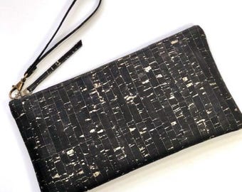 Pode incluir: Bolsa de mão preta e branca com alça de pulso. A bolsa retangular tem um padrão texturizado de formas pequenas e irregulares. O zíper e a alça de pulso são pretos e os acessórios são dourados.