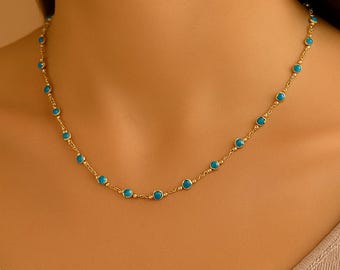May include: A delicate gold necklace featuring small, round, turquoise-colored beads evenly spaced along a fine chain. The necklace is displayed on a person's neck, showcasing its design and color contrast.