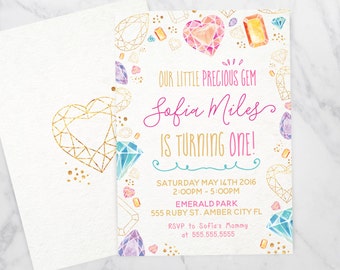 Peut inclure: Une invitation d'anniversaire rose et or avec un motif aquarelle de pierres précieuses colorées. L'invitation indique "Notre petit joyau précieux Sofia Miles a un an !" avec la date et l'heure de la fête, le lieu et les informations RSVP.