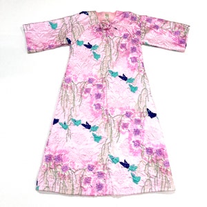 May include: A pink quilted robe with a floral and butterfly pattern. The robe features a tie closure at the neckline and three-quarter sleeves. The design includes purple flowers, teal and navy blue butterflies, and silver-colored vines.