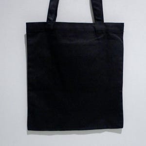 May include: A Cleveland Museum of Art, Yayoi Kusama pumpkin black tote bag with two matching handles. The bag is rectangular and appears to be made of a canvas like fabric. The handles are attached at the top of the bag.