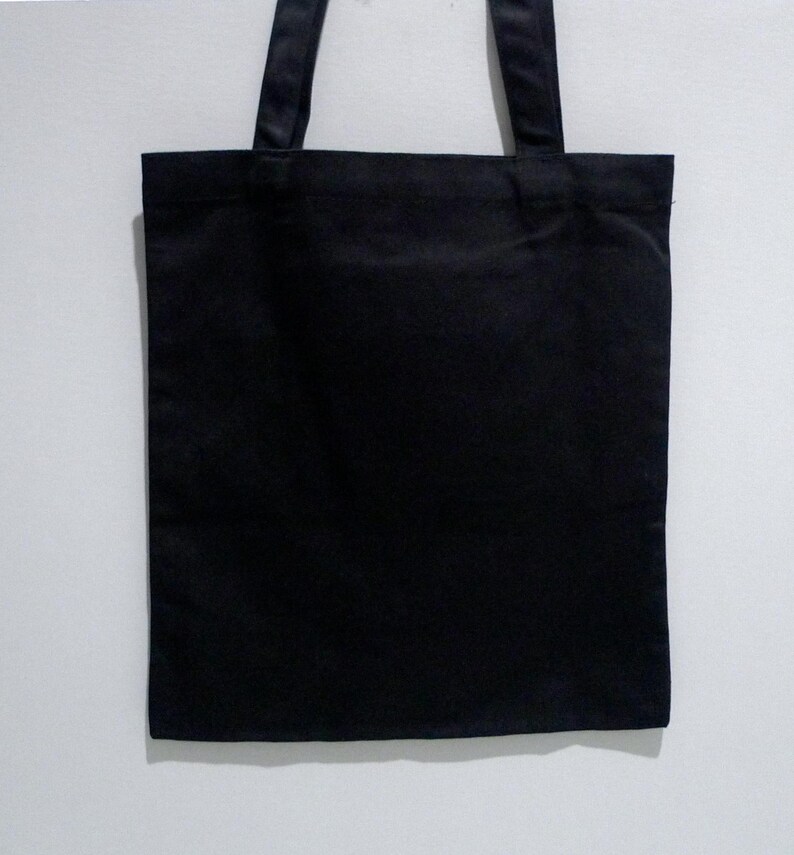 May include: A Cleveland Museum of Art, Yayoi Kusama pumpkin black tote bag with two matching handles. The bag is rectangular and appears to be made of a canvas like fabric. The handles are attached at the top of the bag.