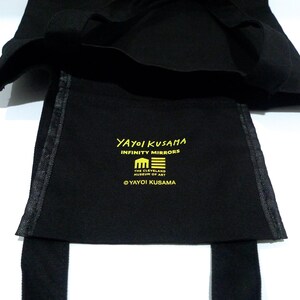 May include: Black tote bag with the text "YAYOI KUSAMA INFINITY MIRRORS" in yellow. The bag also features the emblem of The Cleveland Museum of Art in Ohio and a pumpkin graphic. The bag has straps.