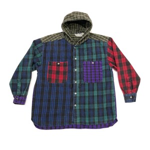 May include: A multi-colored plaid hooded shirt. The shirt features a patchwork design with red, purple, green, and blue plaid patterns. It has two front pockets and a button-up closure. The hood is a darker green, and the cuffs are purple.