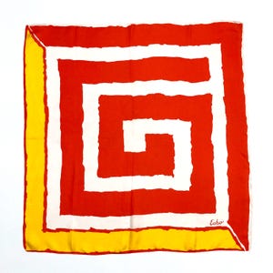 May include: Square silk scarf with a bold geometric design. The scarf features a red spiral pattern with white accents, framed by a yellow border. The word "Echo" is printed in the lower right corner.