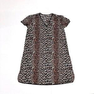 May include: A short-sleeved dress with a V-neckline, featuring a leopard print pattern in shades of brown, black, and cream. The dress has a loose, flowing silhouette and is made of a lightweight fabric, suitable for warm weather.