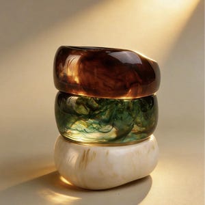 Puede incluir: Tres pulseras apiladas de resina en tonos marrón, verde y crema. La pulsera superior es marrón oscuro, la del medio verde y la inferior crema. Cada pulsera tiene un efecto veteado. Las pulseras son lisas y brillantes.