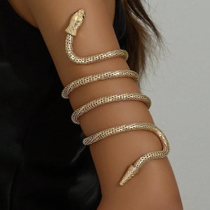 May include: Gold-toned arm cuff in the shape of a snake. The snake's head and tail are detailed with textured scales. The body of the snake wraps around the arm in multiple coils, creating a striking and unique accessory. The jewelry is designed to be worn on the upper arm.