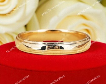 May include: A gold-colored ring with a polished finish. The ring is set on a red surface, with a blurred background of white flowers. The ring has a simple, classic design, suitable for various occasions.