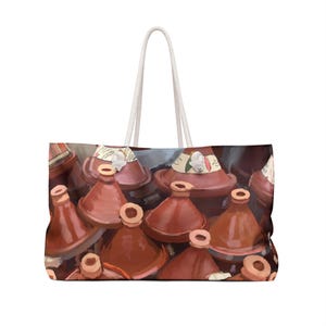 May include: A large tote bag featuring a print of numerous terracotta tagines. The tagines are various sizes and have a reddish-brown color. The bag has a white rope handle, perfect for carrying groceries or other items.