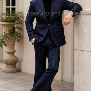 Puede incluir: Traje de raya diplom&aacute;tica azul marino con cuello alto negro. La chaqueta del traje tiene un cierre de un solo bot&oacute;n. Los pantalones son acampanados. The Groom House est&aacute; impreso en la imagen.