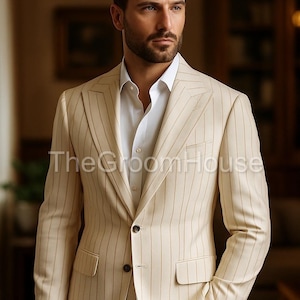 Puede incluir: Traje de rayas finas beige con camisa blanca. La chaqueta del traje tiene dos botones y solapa con muescas. El texto "The GroomHouse" es visible en la chaqueta. El traje es de estilo clásico.