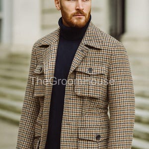 May include: A brown and black checked jacket with four front pockets and two black buttons. The jacket is worn over a navy blue roll-neck sweater. The Groom House logo is visible on the jacket.