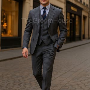Puede incluir: Un traje de tres piezas gris con rayas finas, con chaleco, camisa y corbata a juego. El traje se lleva con zapatos de vestir de cuero marrón. El logotipo de The Groom House es visible en la imagen.