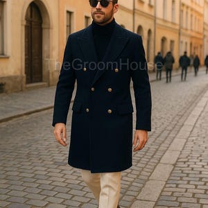 Könnte beinhalten: Ein marineblauer, zweireihiger Mantel mit goldenen Knöpfen. Der Mantel wird über einem schwarzen Rollkragenpullover getragen und mit einer cremefarbenen Hose kombiniert. Das Bild ist auf einer Kopfsteinpflasterstraße aufgenommen.