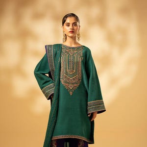 Pode incluir: Um conjunto de túnica e lenço verde-azulado com bordados dourados intrincados. O conjunto é combinado com calças de perna larga roxas escuras com um padrão paisley em vermelho e dourado. A túnica tem mangas compridas.