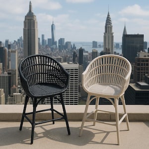 May include: Two bar-height chairs with woven backs and seats. One chair is black, the other is off-white. The chairs have a curved back design and are supported by four legs. The chairs are on a rooftop with a cityscape in the background.
