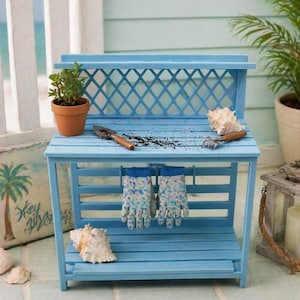 May include: A light blue potting bench with a lattice back, holding a small potted plant, gardening tools, and a pair of floral print gloves. Seashells are placed around the bench. The bench is made of wood and has a slatted shelf.