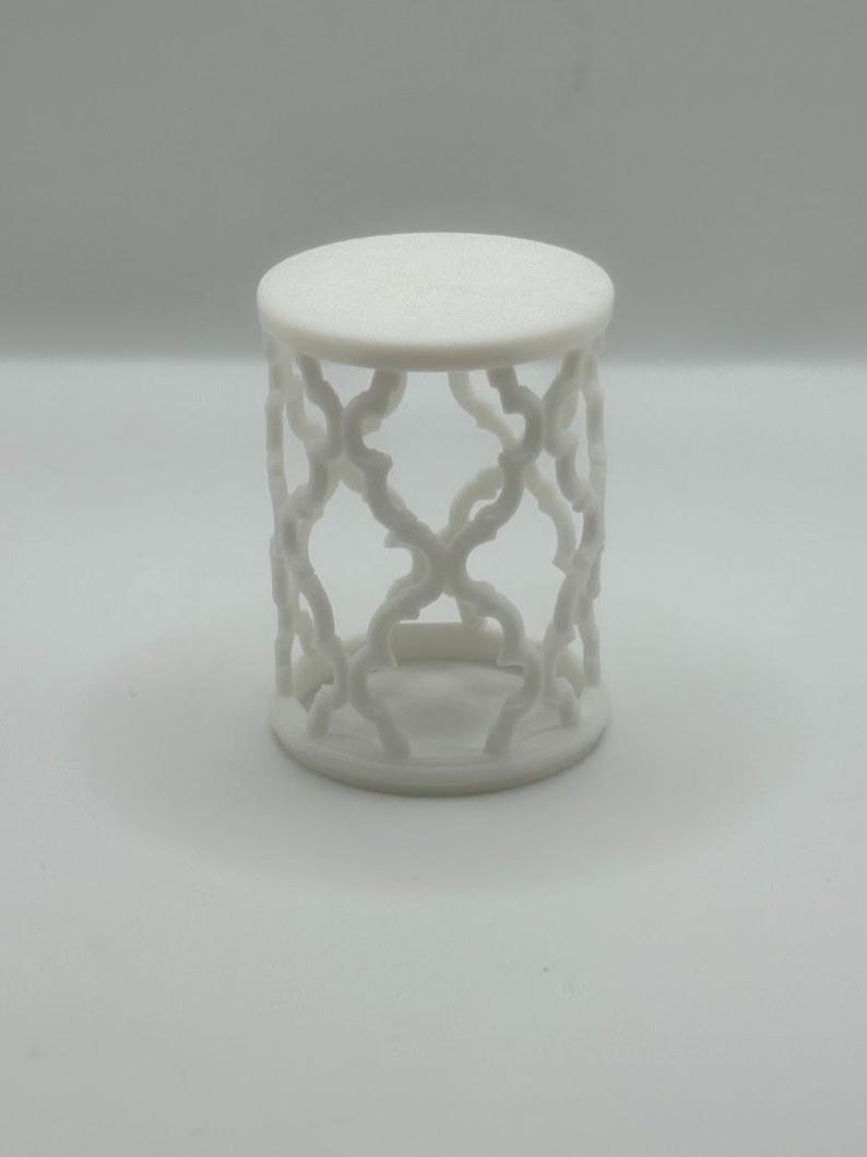 Pu&ograve; includere: Tavolino decorativo bianco, con piano rotondo e design traforato a griglia sui lati. Il tavolino &egrave; alto circa 25 cm e ha un diametro di 20 cm, adatto per esporre piccoli oggetti.