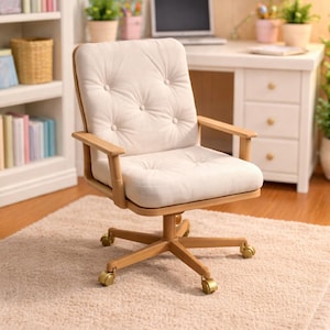 May include: A miniature office scene featuring a cream-colored upholstered desk chair with a tufted back and wooden frame. The chair has gold-colored casters and sits on a beige rug. A white desk and bookshelf are in the background.