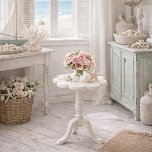 May include: A coastal-themed interior with a white and light blue color scheme. A small white table holds a bouquet of pink roses. A wicker basket with flowers and starfish sits nearby. A model sailboat and coral decor are on a side table.