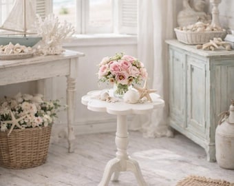 Puede incluir: Un interior de temática costera con una combinación de colores blanco y azul claro. Una pequeña mesa blanca sostiene un ramo de rosas rosas. Una cesta de mimbre con flores y estrellas de mar está cerca. Un modelo de velero y decoración de coral están en una mesa auxiliar.