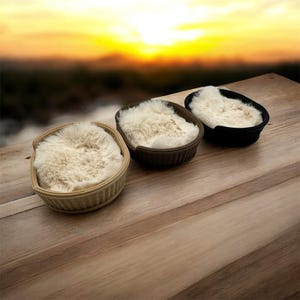 以下が含まれることがあります： 3つの小さなペット用ベッドが並んでおり、それぞれ異なる色の織りバスケットとふわふわのクリーム色の内装が施されています。バスケットは薄いベージュ、茶色、黒です。ベッドは木製の表面に置かれ、背景にはぼやけた夕焼けが見えます。