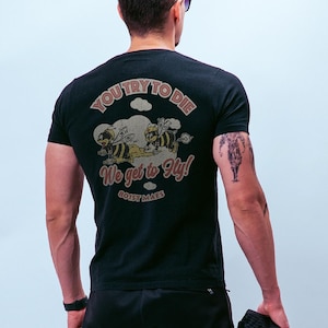 May include: Black t-shirt with a graphic featuring two cartoon bees and the text "You try to die, We get to fly!" and "BOIST MAES" in a vintage style. The shirt is short-sleeved.