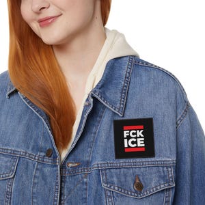 Könnte beinhalten: Eine blaue Jeansjacke mit einem schwarzen Aufnäher mit der Aufschrift "FCK ICE" in weißen Buchstaben und roten Linien. Die Jacke hat einen Kragen und eine Knopfleiste.