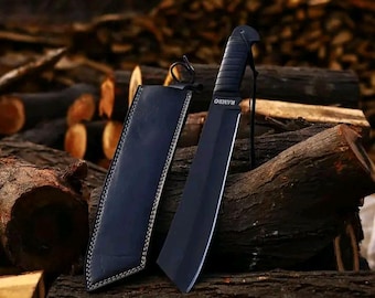 May include: A black machete with the word "RAMBO" printed on the blade, and a black leather sheath. The knife is resting on a pile of wood logs. The handle is textured for grip.