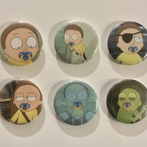 Puede incluir: Conjunto de seis botones redondos con personajes de dibujos animados con chupetes. Los personajes, incluido Morty, están representados en varias poses y colores. Los botones están sobre una superficie blanca.
