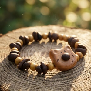 Può includere: Braccialetto in legno con un ciondolo a forma di orso e perline marrone scuro e marrone chiaro alternate. Il ciondolo a forma di orso ha un naso marrone scuro e una bocca sorridente. Il braccialetto è appoggiato su una superficie di legno.
