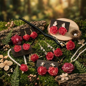 Può includere: Una collezione di gioielli con motivi a rosa rossa, tra cui orecchini, un fermaglio per capelli e una collana con perle bianche. Il set include diverse paia di orecchini a forma di rosa, una lunga forcina nera e una collana con un ciondolo.