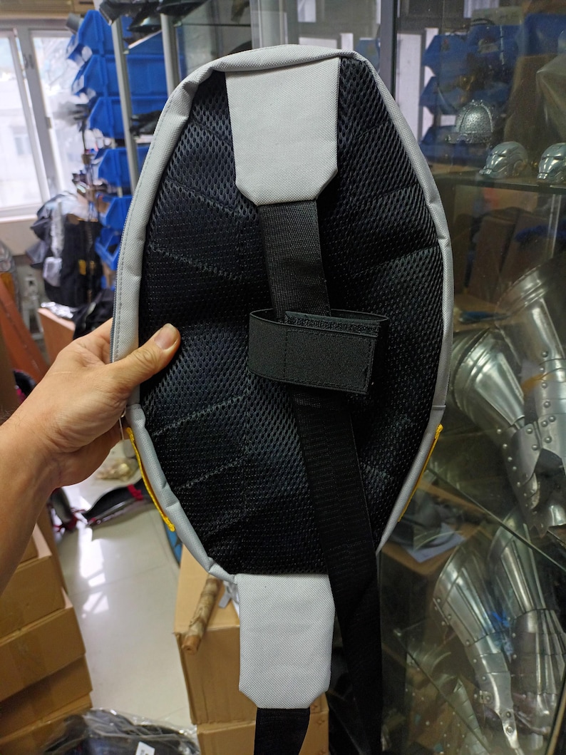 May include: A gray and black sling backpack with a padded back panel and adjustable strap. The backpack features a mesh back for breathability and a gray accent on the top and bottom. The strap has a velcro closure.