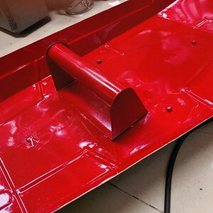K&ouml;nnte beinhalten: Eine leuchtend rote Metallschale mit einem gebogenen Griff. Die Schale hat eine rechteckige Form mit quadratischen Vertiefungen. Der Griff ist ein abgerundetes Rechteck. Die Oberfl&auml;che ist gl&auml;nzend.