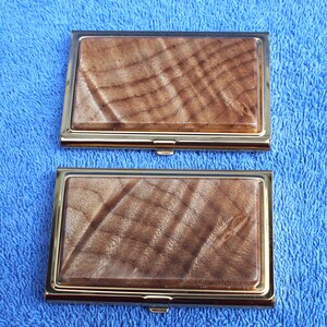 May include: Two gold-trimmed business card holders with a wood grain pattern. The wood grain is a light brown with darker brown streaks.