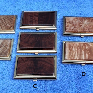 May include: Five different wooden business card holders with gold trim. The holders are arranged in a row, with the top row having two holders and the bottom row having three holders. The holders are made of different types of wood, including maple, walnut, and cherry. The holders are all in a horizontal orientation.