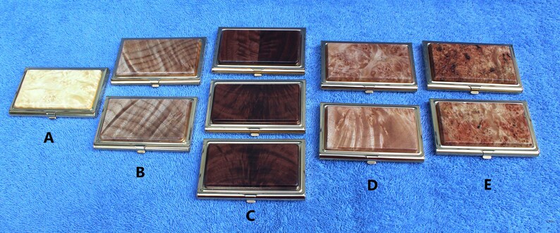 May include: Five different wooden business card holders with gold trim. The holders are arranged in a row, with the top row having two holders and the bottom row having three holders. The holders are made of different types of wood, including maple, walnut, and cherry. The holders are all in a horizontal orientation.