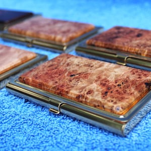 May include: A set of six wooden business card holders with a gold metal frame. The holders are made of different types of wood with unique grain patterns.